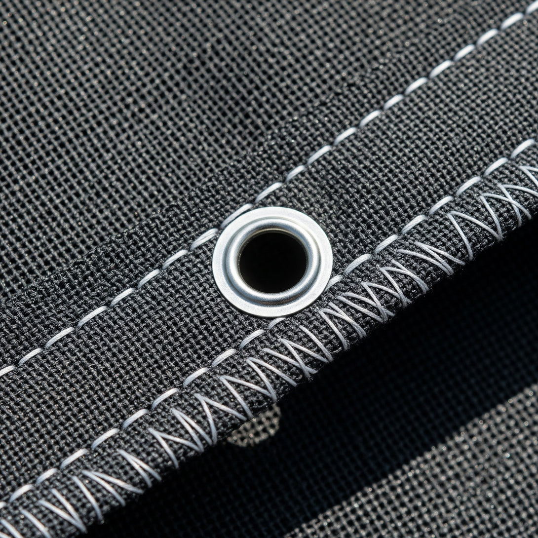 Close-up of gray shade cloth fabric with white stitching and a metal grommet.