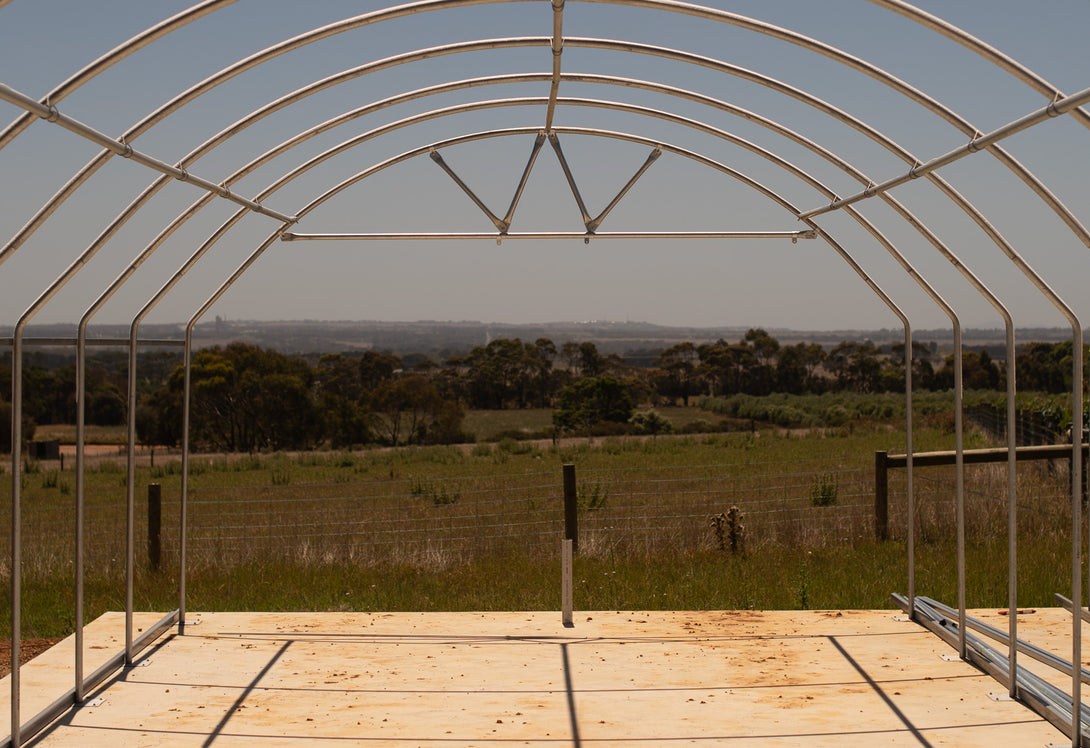 Metal arch structure with wooden floor, open to a scenic landscape.