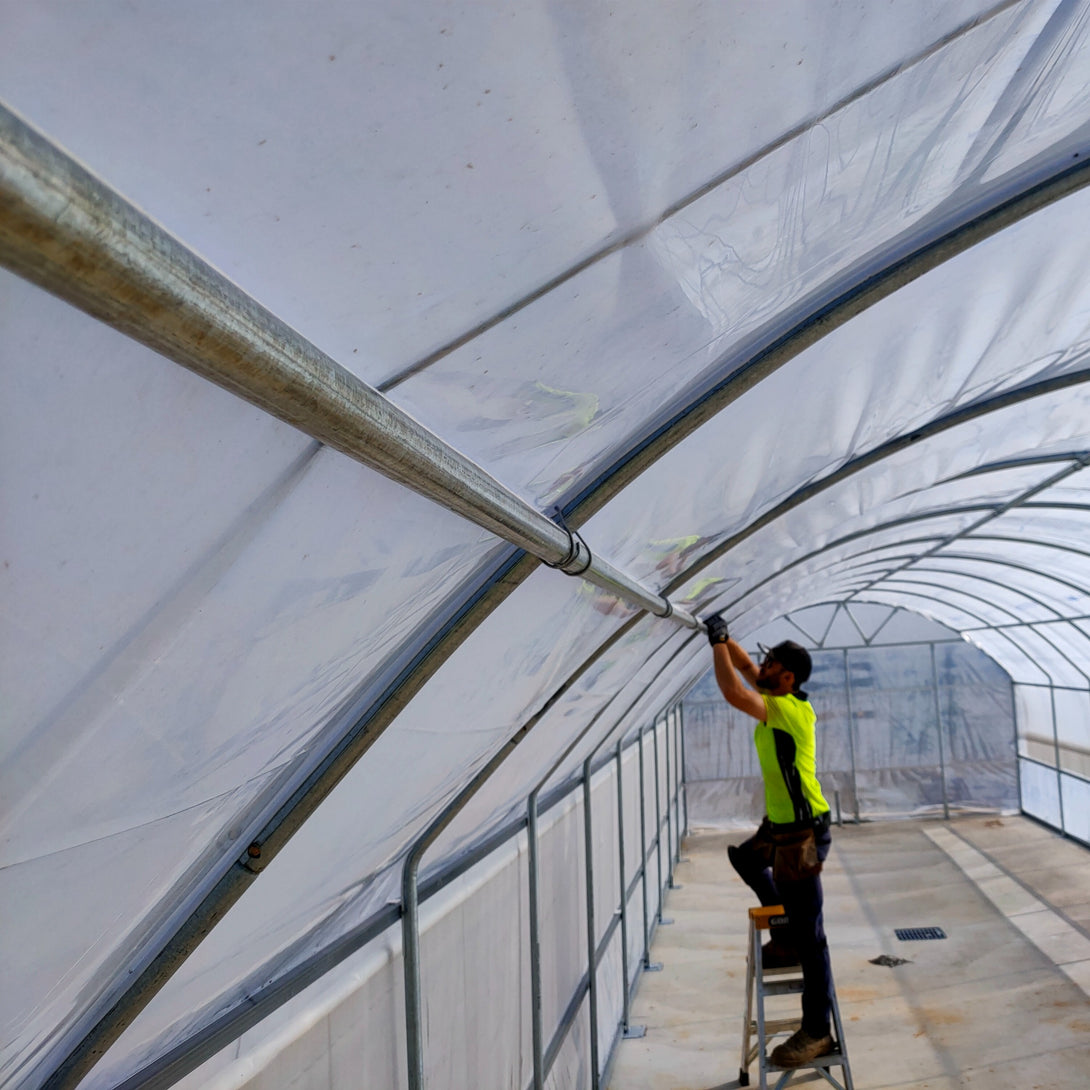 Person working on a large white tent structure inside a greenhouse.